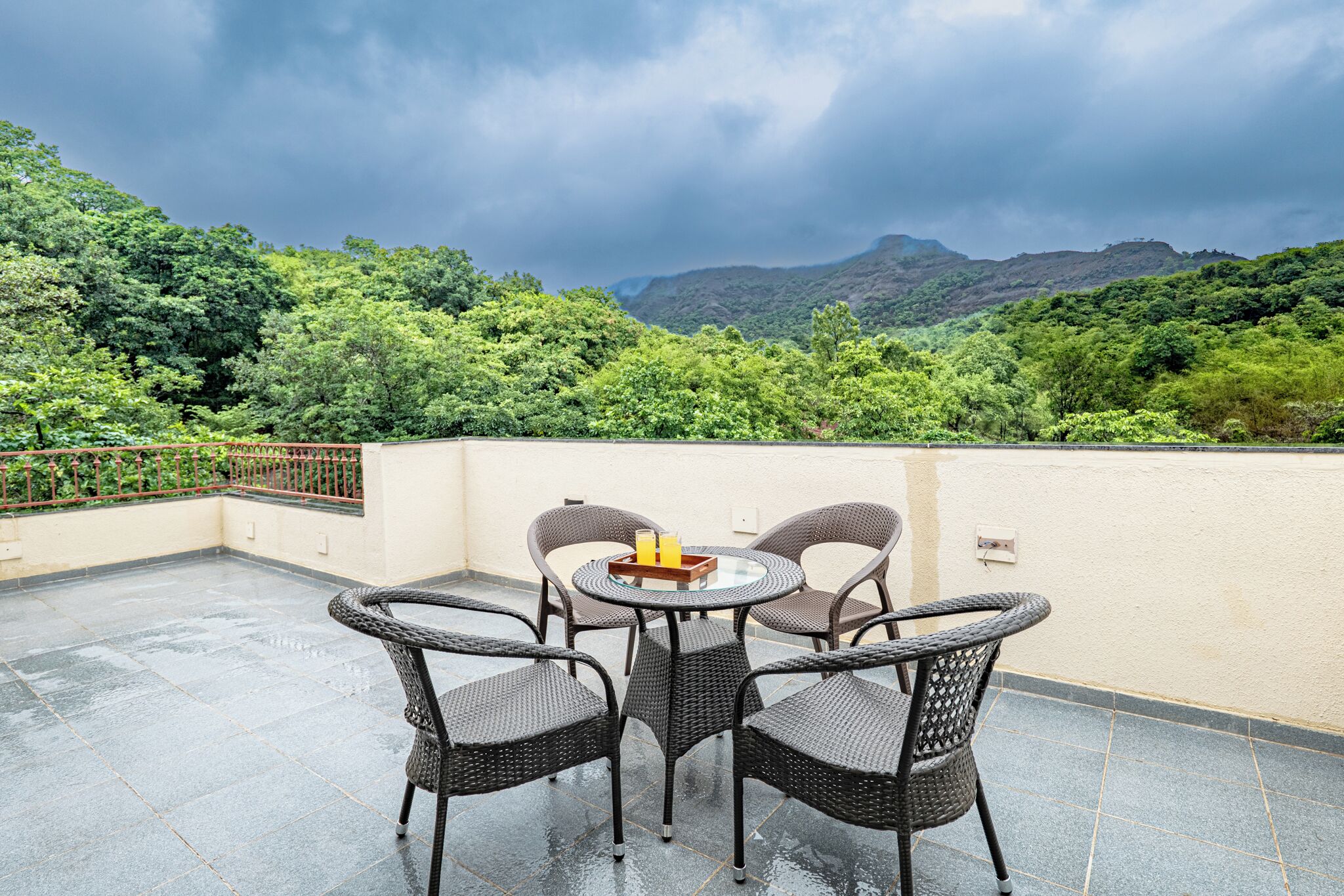 Una terraza con mobiliario de mimbre y una mesa, con vistas a un paisaje verde exuberante y montañas.
