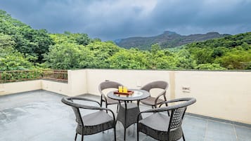Una terraza con mobiliario de mimbre y una mesa, con vistas a un paisaje verde exuberante y montañas.