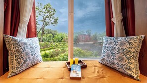 A bed with two patterned pillows, a tray with a book and two glasses, and a view of a garden through a window. - CosmicStays Yutori  (Mulshi)