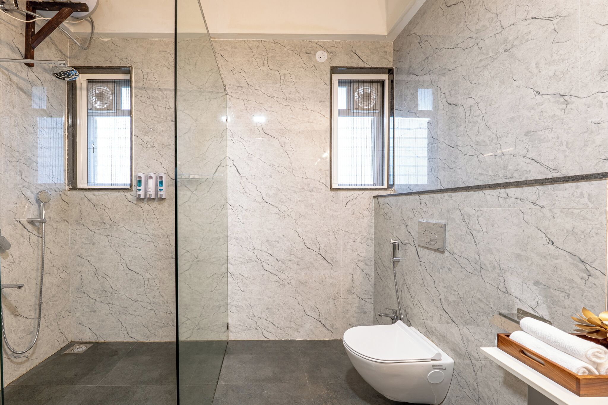Et moderne badeværelse med et glasvægshus, toilet og et håndvaskområde med håndklæder.