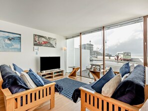 A living room with a TV, wooden furniture, and a large window overlooking a street. - 1 Bed in Bideford (oc-poinb) (Westward Ho!)