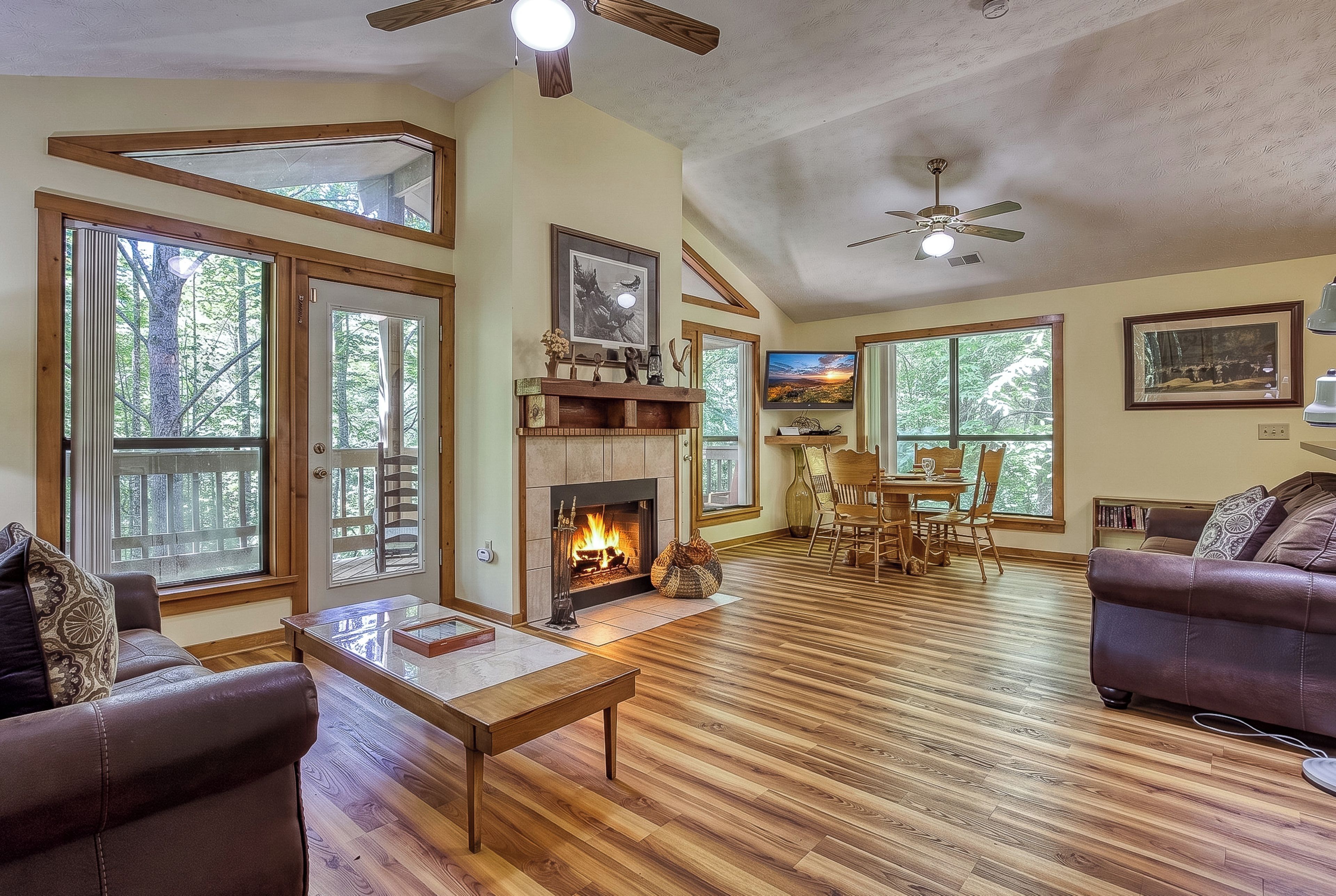 A spacious living room with a fireplace, wooden flooring, and large windows.