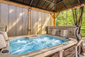 Ein Whirlpool mit Holzterrasse und Metallveranda, umgeben von einem Holzzaun und Grünpflanzen.