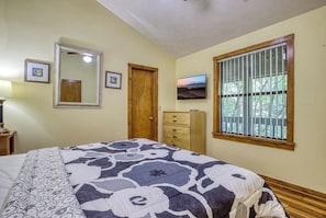 Ein Schlafzimmer mit einem Bett, einem Schminktisch, einem Spiegel, einem Fernseher und einem Fenster mit Jalousien.
