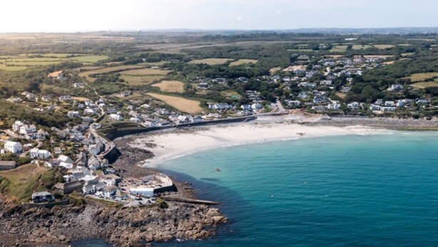 Uma cidade costeira com uma praia arenosa, costa rochosa e edifícios residenciais.