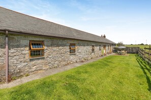 A stone building with multiple windows, a grassy yard, and a wooden fence. - 3 Bed in Falmouth (oc-conwi) (Constantine)