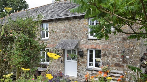 A stone house with a garden in front, featuring a variety of flowers and plants. - 2 Bed in Wadebridge (oc-jobes) (Chapel Amble)