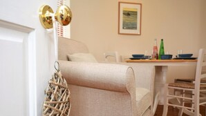 Ein beiges Sofa, ein Korbstuhl, ein Esstisch mit Stühlen und ein gerahmtes Bild an der Wand.
