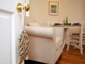 Ein beiges Sofa, ein Korbstuhl, ein Esstisch mit Stühlen und ein gerahmtes Bild an der Wand.