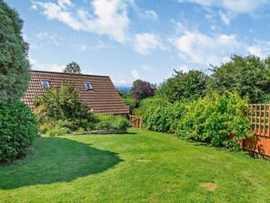 Ein Haus mit geneigtem Dach, einem eingezäunten Garten und viel Grün.