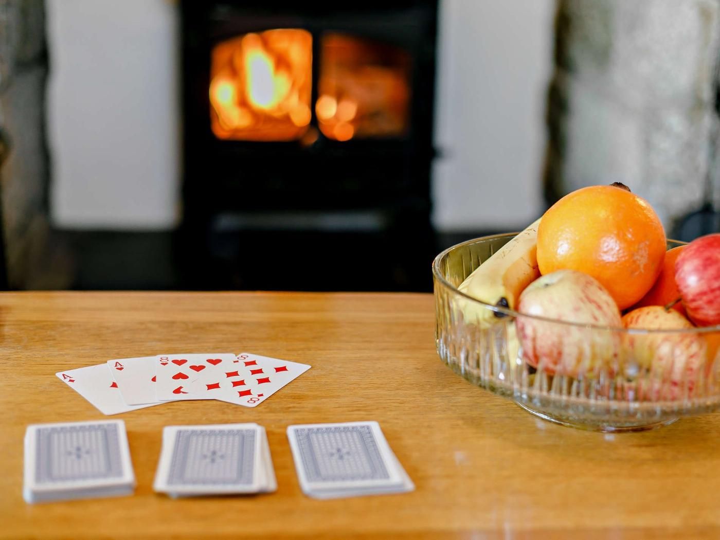 Une table en bois, avec un jeu de cartes et un saladier rempli de fruits.