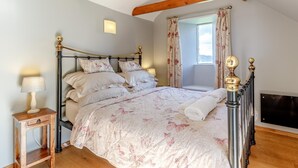Une chambre à coucher avec un lit, une table de chevet, une fenêtre avec des rideaux et des poutres apparentes en bois.