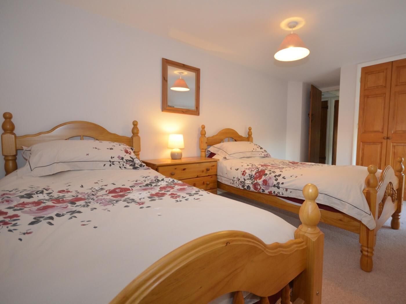 A bedroom with two wooden beds, a bedside table with a lamp, a mirror on the wall, and a wooden wardrobe.