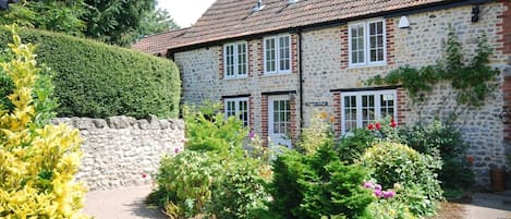 A stone building with a tiled roof, a stone wall, and a paved driveway.