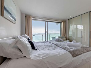 Ein Hotelzimmer mit Bett, Sessel, einem Balkon mit Meerblick und einer Schiebeglastür.