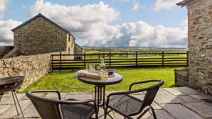 A patio with a round table and two chairs, a stone building, and a grassy field with a fence in the background. - 1 Bed in Bideford (oc-linne) (Hartland)