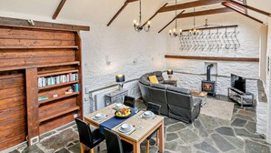 A cozy room with a stone floor, a fireplace, a sofa, a dining table set for four, and a bookshelf. - 1 Bed in Camelford (oc-hopar) (Lanteglos)