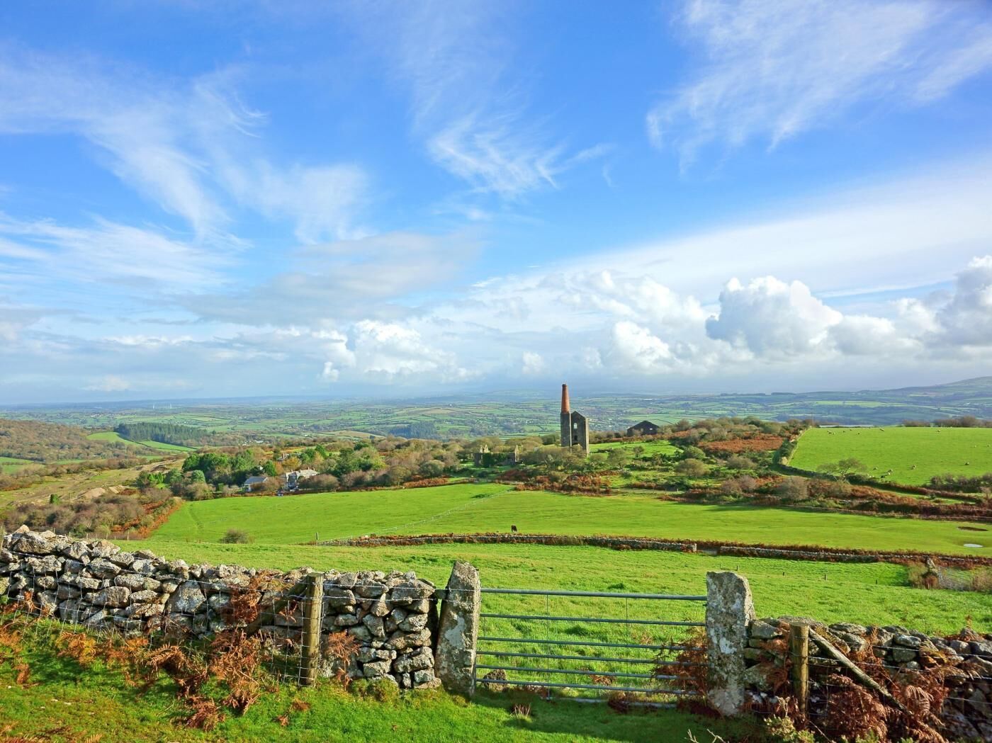 A rural landscape with a stone wall, a metal gate, and a distant church.
