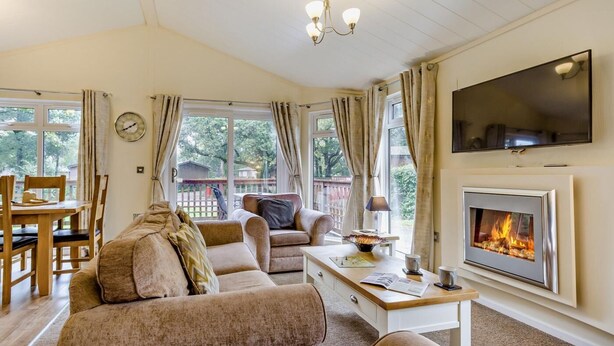 A cozy living room with a fireplace, comfortable seating, a dining area, and a TV mounted on the wall. - 3 Bed in Okehampton (oc-06199) (Okehampton Hamlets)