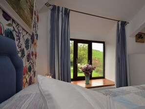 A bedroom with a bed, a window with curtains, a vase with flowers, and a painting on the wall. - 2 Bed in Ivybridge (oc-kemth) (Ugborough)