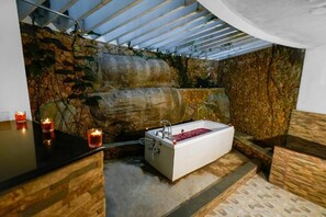 A bathroom with a bathtub, stone walls, and a wooden counter.