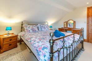 Ein Schlafzimmer mit einem Bett, Nachttischen, einer Kommode, einem Spiegel und einer Tür.