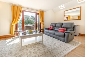 Ein Wohnzimmer mit einer Couch, einem Couchtisch und Blick durch eine Glastür auf einen Außenbereich.