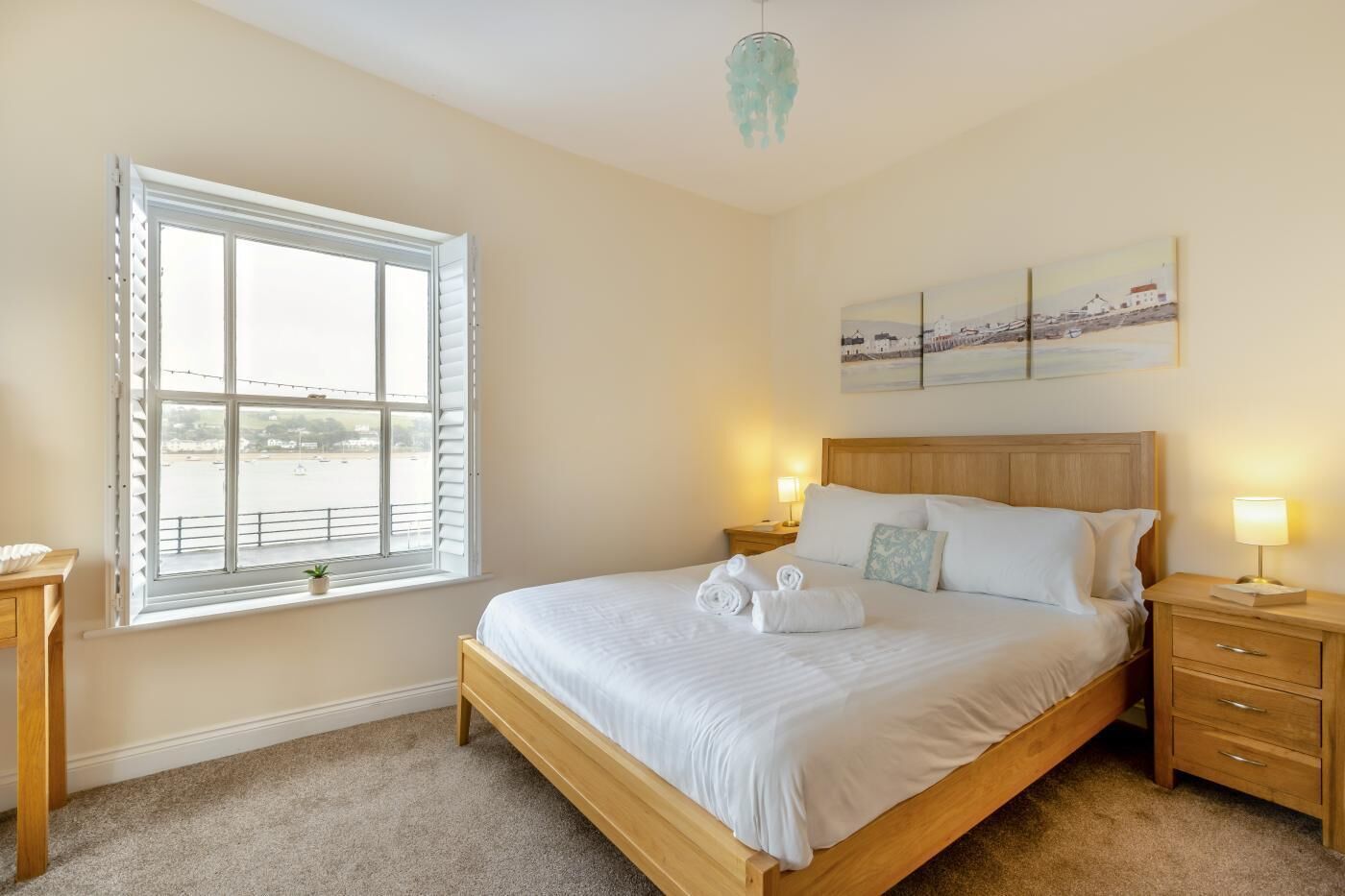 A bedroom with a large window, a bed, bedside tables, and a wall-mounted artwork.