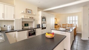 A modern kitchen with white cabinetry, a granite countertop, and a dining area with wooden chairs. - 2 Bed in Bideford (oc-05208) (Appledore)