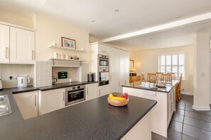 A modern kitchen with white cabinetry, a granite countertop, and a dining area with wooden chairs. - 2 Bed in Bideford (oc-05208) (Appledore)