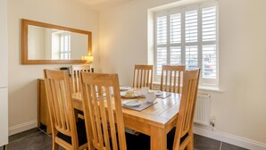 A dining area with a wooden table and chairs, a mirror on the wall, and a window with blinds. - 2 Bed in Bideford (oc-05208) (Appledore)