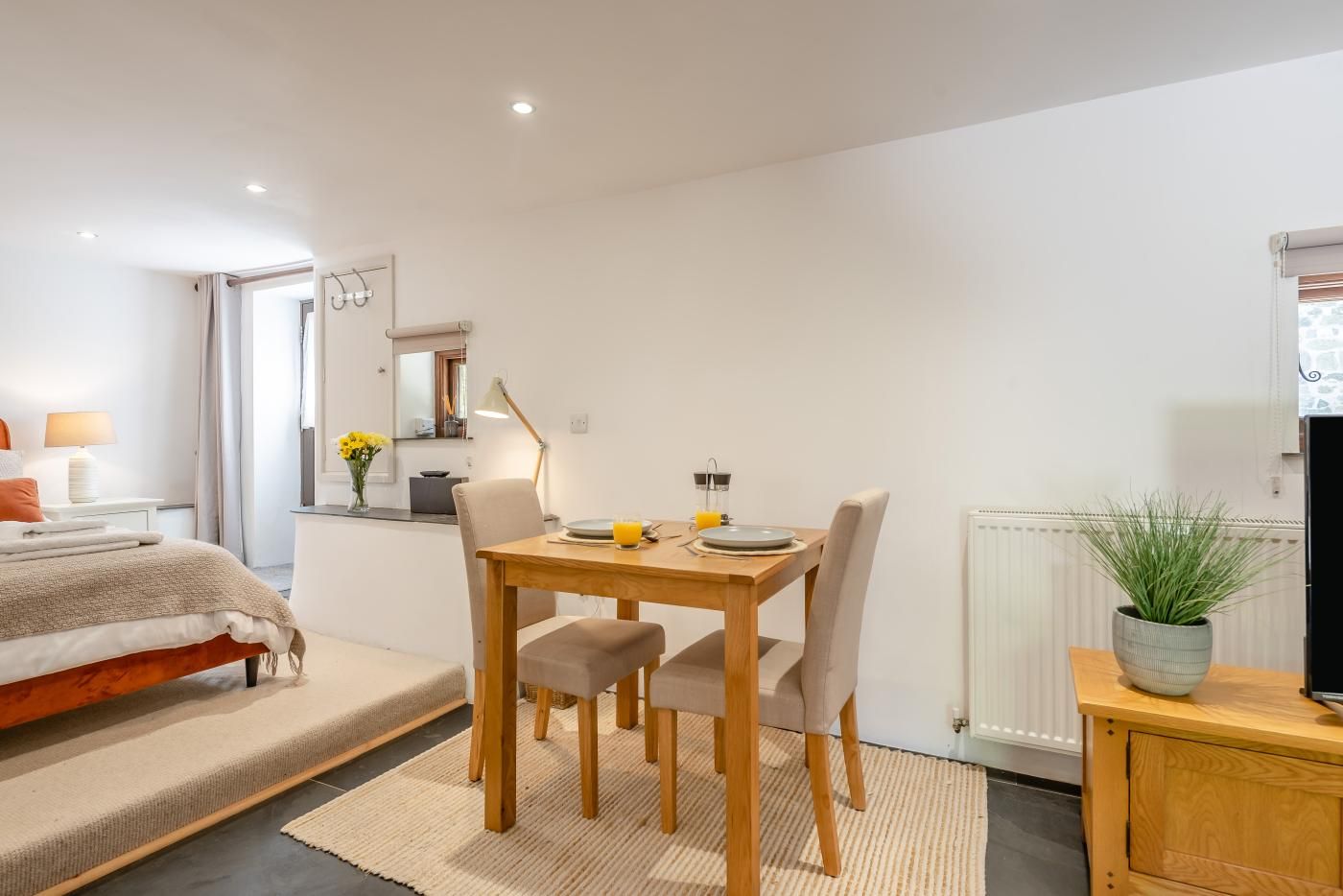 Une chambre à coucher moderne avec un lit, une table de chevet, une lampe et une petite table à manger avec des chaises.