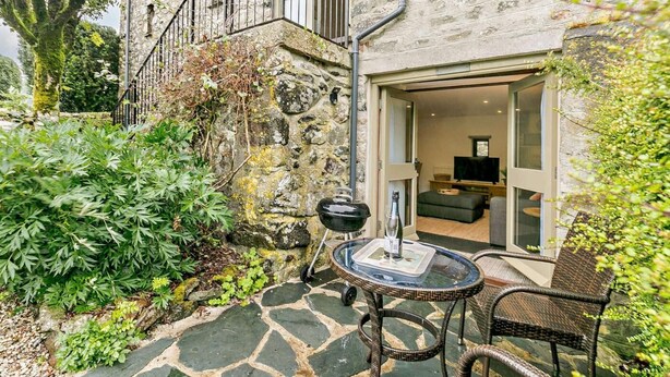 A stone building with a staircase leading to a balcony, a glass door entrance, a small outdoor seating area with a table and chair, and a television in the interior. - 1 Bed in Tavistock (oc-hgard) (Cudlipptown)