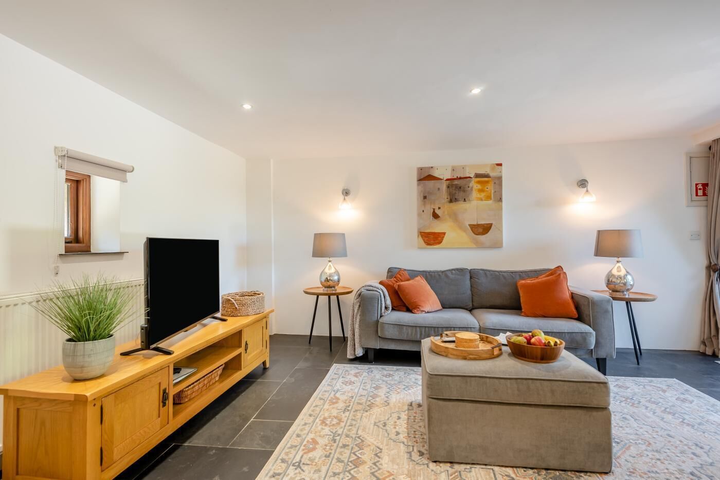 Ein modernes Wohnzimmer mit Flachbildfernseher, grauem Sofa und einem Couchtisch mit Obst.