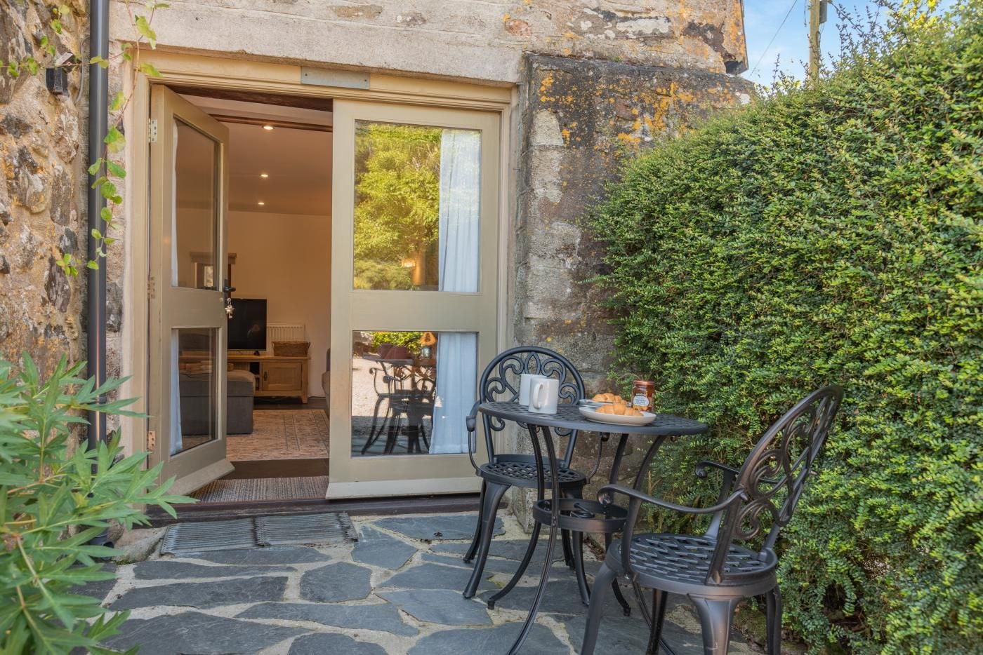 An outdoor patio with a table and chairs, a door leading to an interior space, and a stone floor.