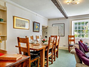 A dining area with a wooden table and chairs, a sofa with cushions, and artwork on the walls. - 4 Bed in Bideford (oc-hacot) (Hartland)
