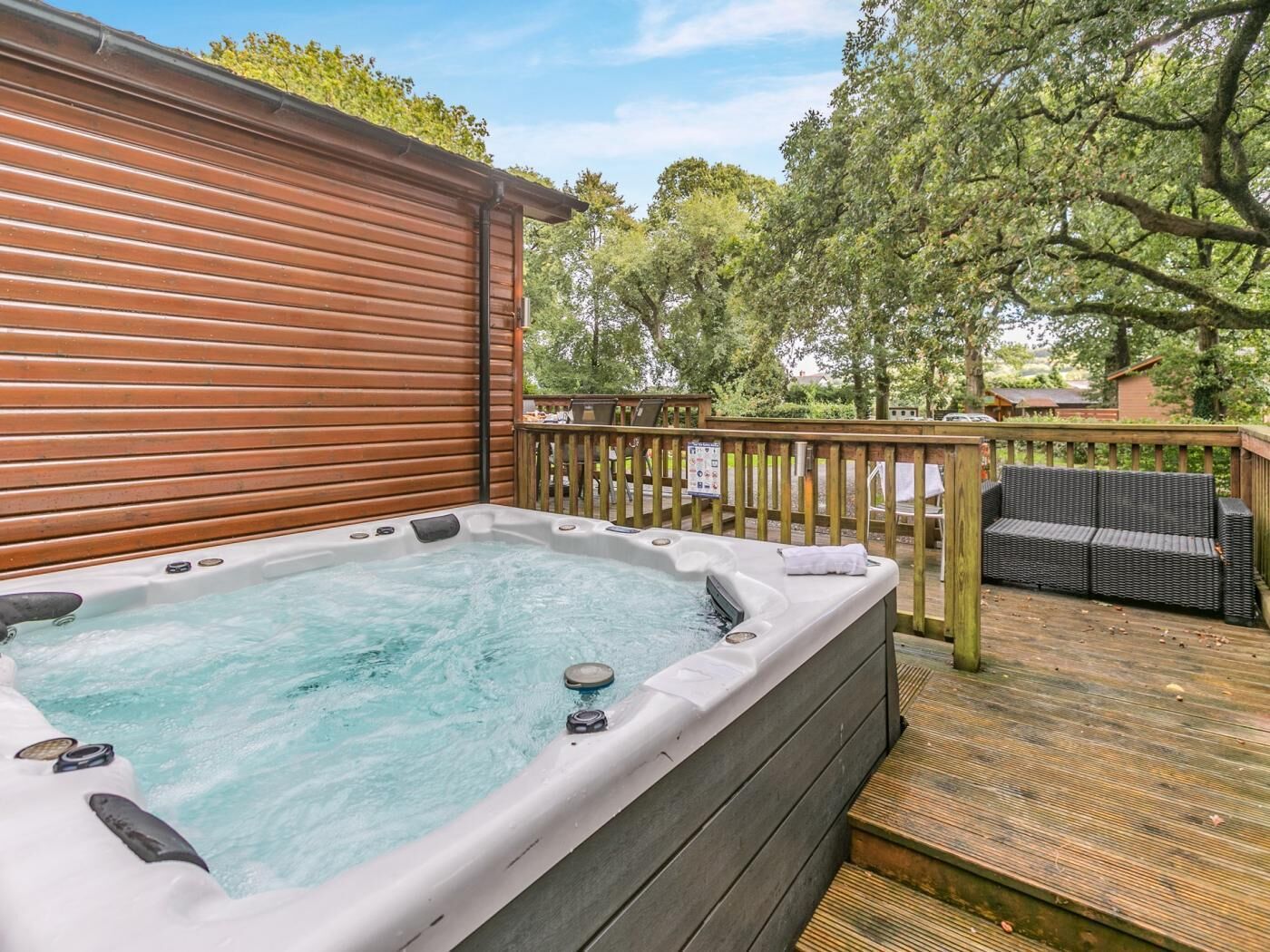 Un bain à remous sur une terrasse en bois, avec une clôture en bois et des meubles d’extérieur.