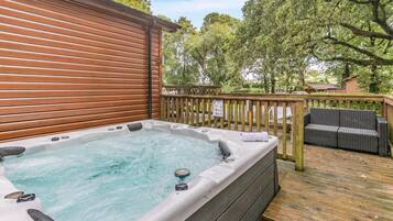 Un bain à remous sur une terrasse en bois, avec une clôture en bois et des meubles d’extérieur.