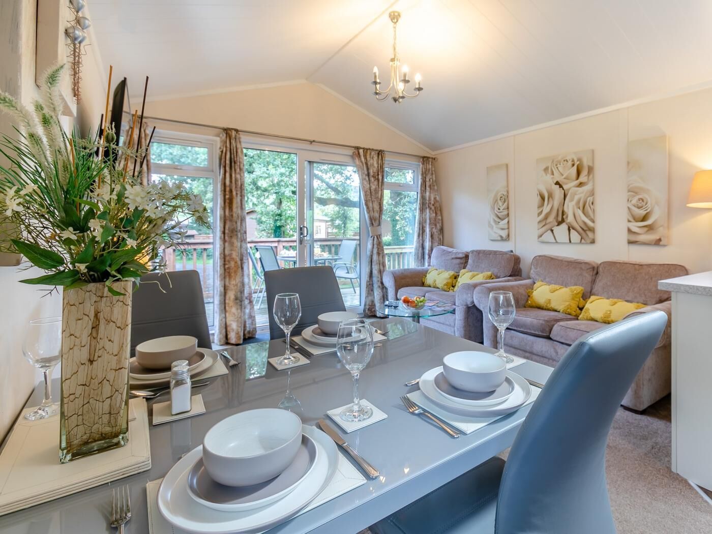 Un coin repas avec une table dressée pour deux personnes, un canapé et un balcon agrémenté de rideaux.