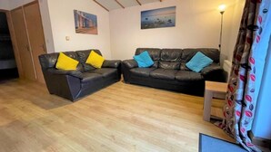 A living room with two black leather sofas, wooden flooring, a ceiling with wooden beams, and a lamp. - 2 Bed in Redruth (oc-gillo) (Scorrier)