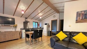 A compact living space with a dining area, a kitchen, a sofa with yellow cushions, and a flat-screen TV. - 2 Bed in Redruth (oc-gillo) (Scorrier)