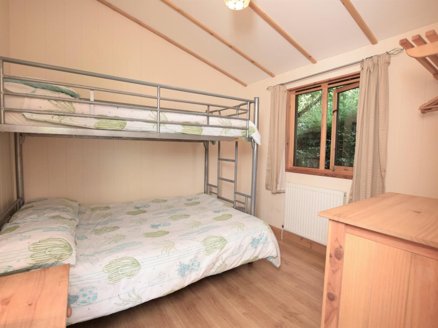 Een slaapkamer met een stapelbed, raam, houten vloer en een klein houten tafeltje.