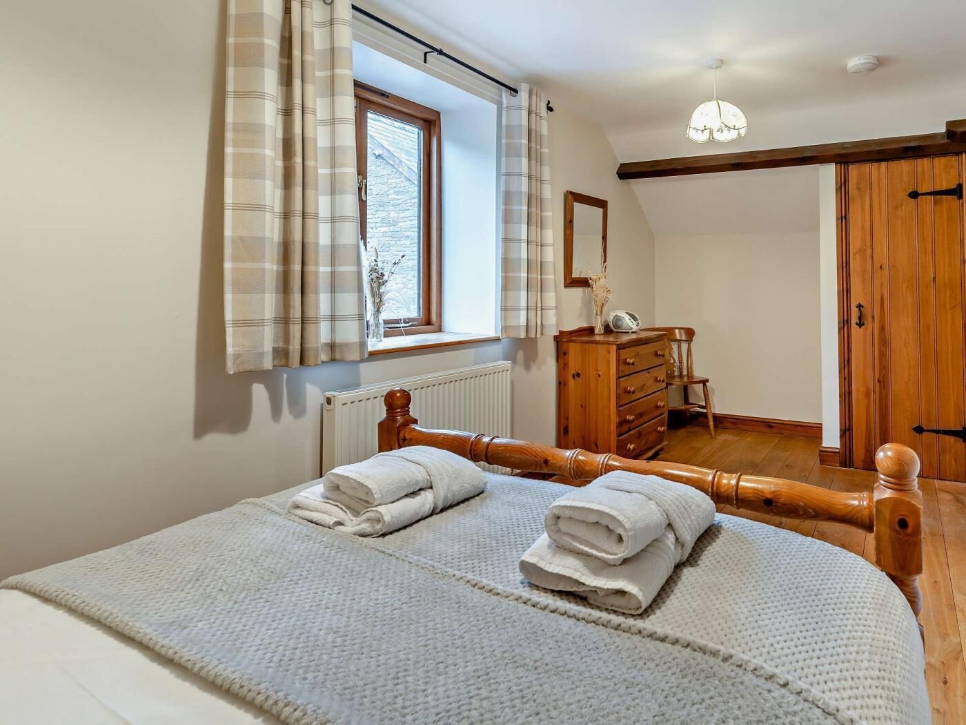 Un dormitorio con cama de madera, cómoda, espejo, ventana con cortinas y puerta.