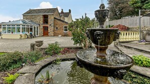 Uma casa de pedra com estufa, uma fonte e um jardim com plantas e um pequeno lago.