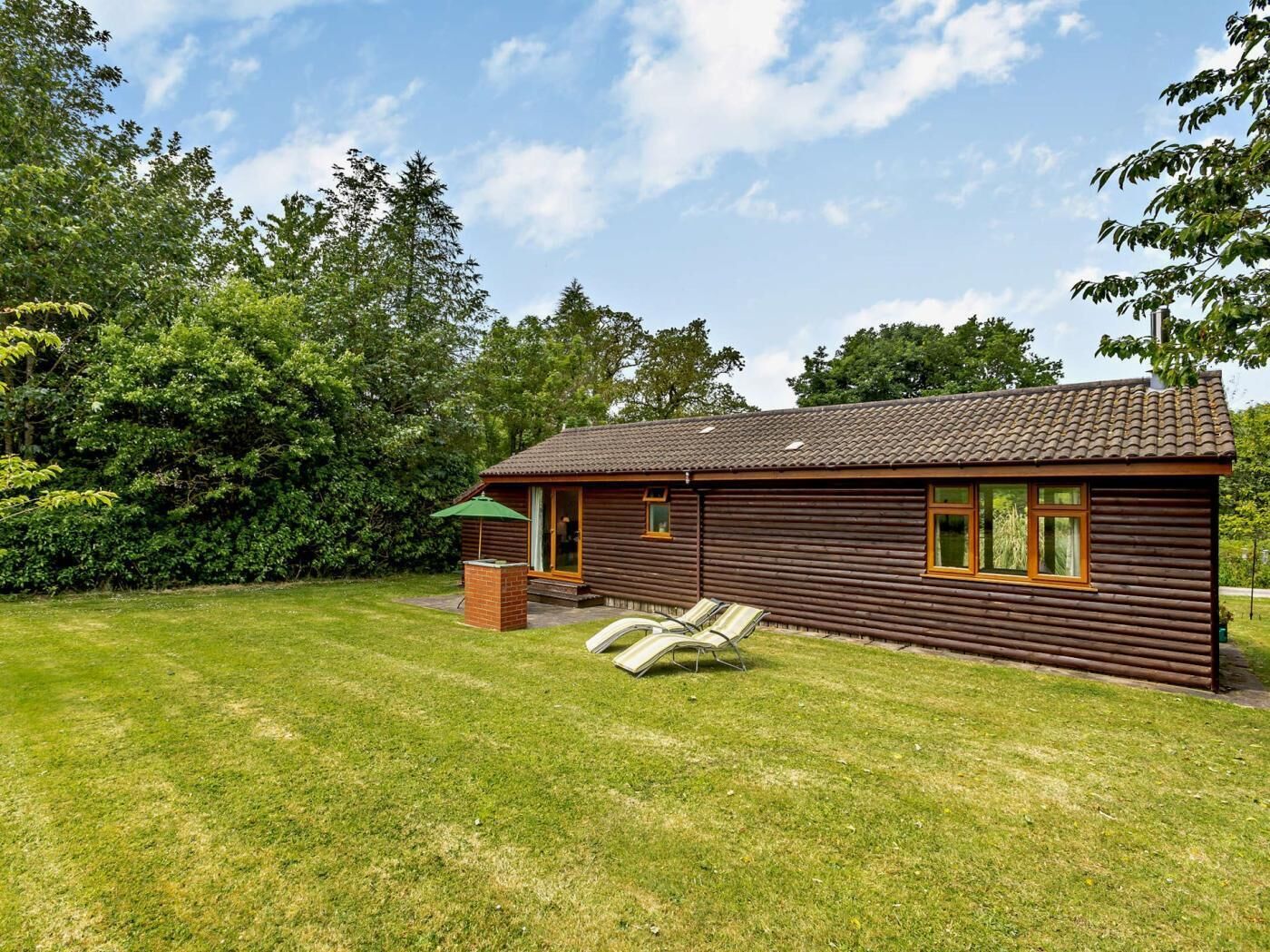 Een vakantiehuisje van hout met pannendak, een klein terrasje met stoel en parasol, en een gazon.