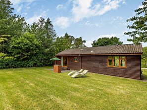 A log cabin with a tiled roof, a small patio with a chair and umbrella, and a grassy yard. - 1 Bed in South Molton (oc-chevi) (South Molton)