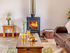 A living room with a wood-burning stove, a wooden table with drinks and pastries, a brown leather sofa, and a wicker basket. - 1 Bed in South Molton (oc-chevi) (South Molton)