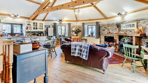 A spacious living area with a high ceiling, wooden beams, a fireplace, a leather sofa, and a dining area with wooden furniture. - 2 Bed in Liskeard (oc-trero) (Menheniot)
