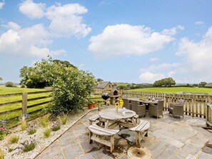 A patio area with a round wooden table and chairs, surrounded by stone flooring. - 4 Bed in Launceston (oc-brhig) (Launceston)