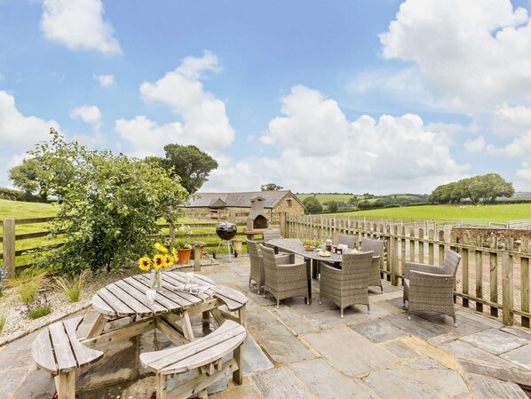 An outdoor patio with stone flooring, wicker furniture, and a view of a stone building in the distance. - 4 Bed in Launceston (oc-brhig) (Launceston)